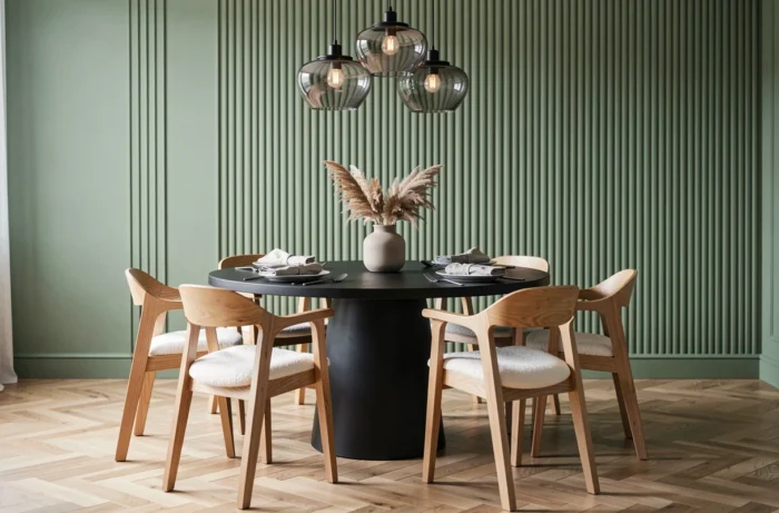 Contemporary dining room with a round black table, oak and boucle chairs, sage green striped wall, and herringbone parquet